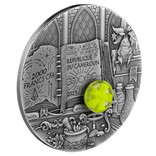 Intricately engraved 2023 Cameroon Wizard 2oz Silver High Relief Antiqued Coin w/3D Insert with Mintage of 888 featuring themes of knowledge and wizardry, including an open book with the text "republic of cameroon 2023," alongside a faceted green gemstone, a.